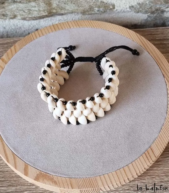 Bracelet à trois rangs de cauris blancs et perles noires sur un présentoir rond